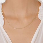 A close-up of a woman’s neck wearing a Custom Gold Necklace in yellow gold with three letter charms, a K and an E on the left side and a B on the right side, and a white blouse.