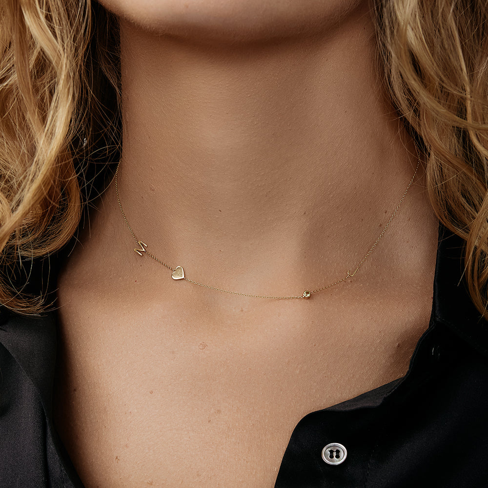 Close-up of a model wearing a delicate gold necklace with initials, a birthstone and a heart charm.