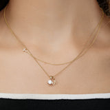 Gold necklace with a small gold letter pendant on a person wearing a black and white top.