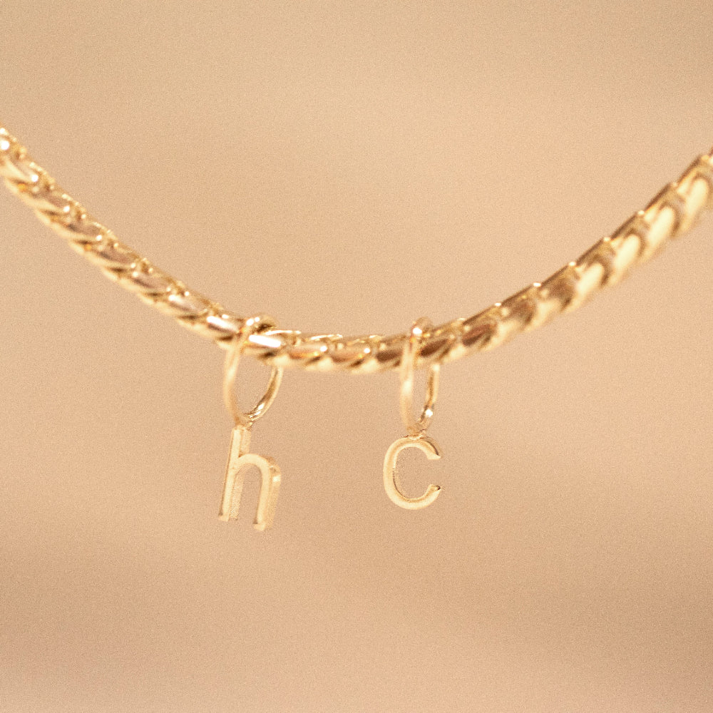 Gold necklace with 'hc' charms on a beige background