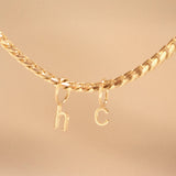 Gold necklace with 'hc' charms on a beige background