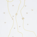 Three gold necklaces with single letter charms, being J, B and W, featuring multiple little gemstones on a white background.