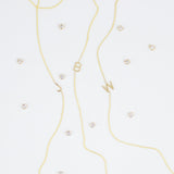 Three gold necklaces with single letter charms, being J, B and W, featuring multiple little gemstones on a white background.