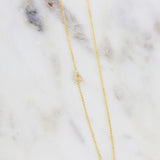 A gold necklace with a pave letter A charm  on a marble background.