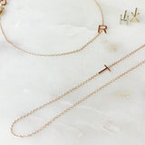 A necklace, bracelet and two stud earrings, each with its own letter charm – R, T, H, and X against an off white marble background.