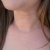 A close-up of a woman's neck wearing a rose gold necklace with a letter T charm.