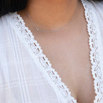 A close-up of a woman's neck wearing a white gold necklace with a letter L charm.
