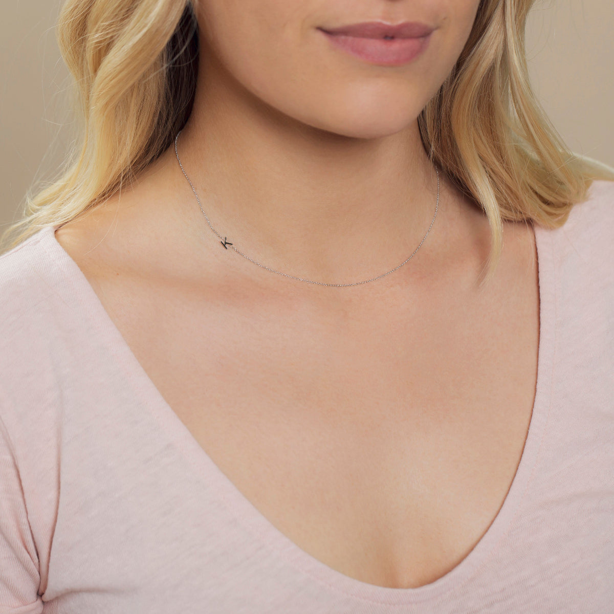 Close-up of a woman's neck wearing a white gold necklace with a letter K charm.