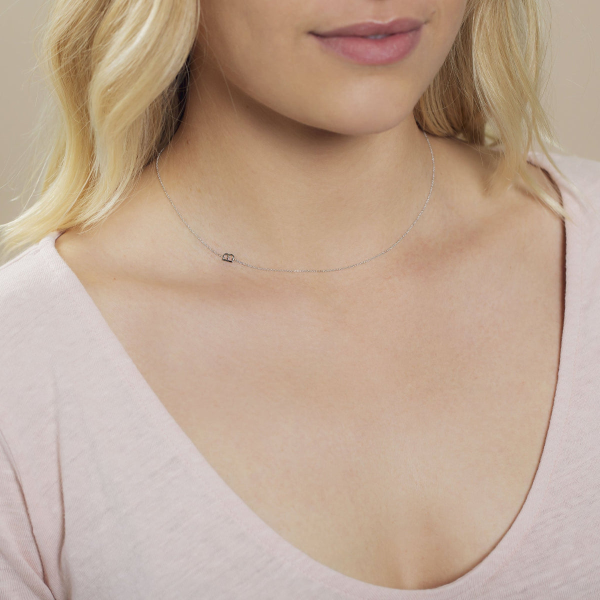 A close-up of a woman's neck wearing a white gold necklace with a letter B charm.