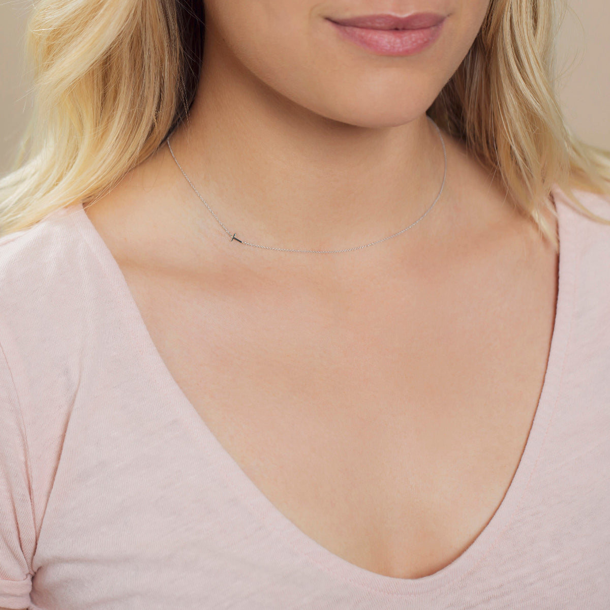 A close-up of a woman's neck wearing a white gold necklace with a letter T charm.