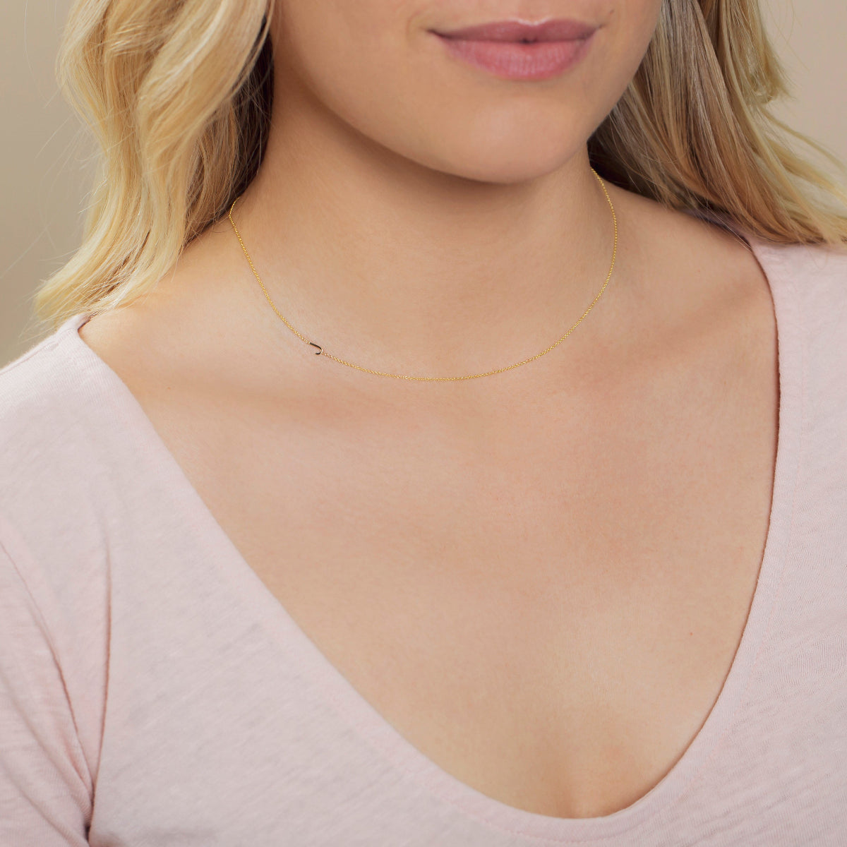 Close-up of a woman's neck wearing a yellow gold necklace with a letter J charm.