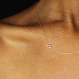 A close up of a woman's décolletage wearing a yellow gold necklace with a letter S charm.