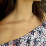 A close-up of a woman’s neck area wearing a yellow gold necklace with a letter S charm and a patterned off-shoulder top.