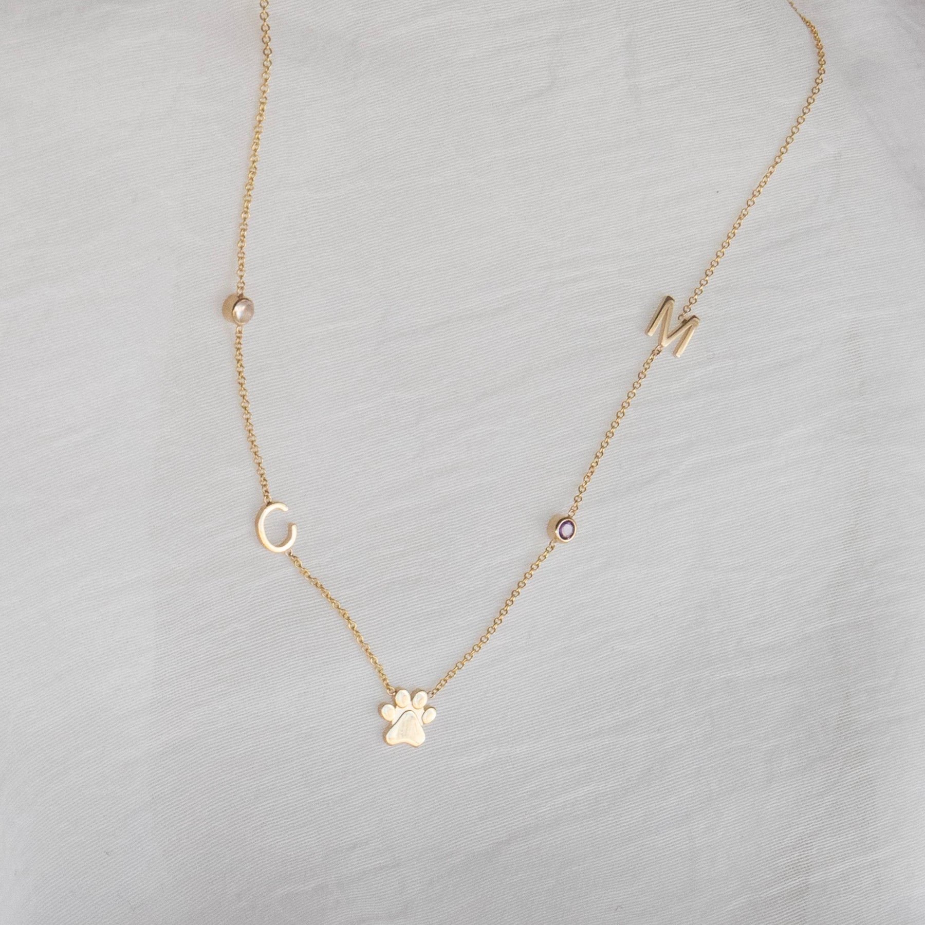 Gold necklace with various charms on a light gray fabric background