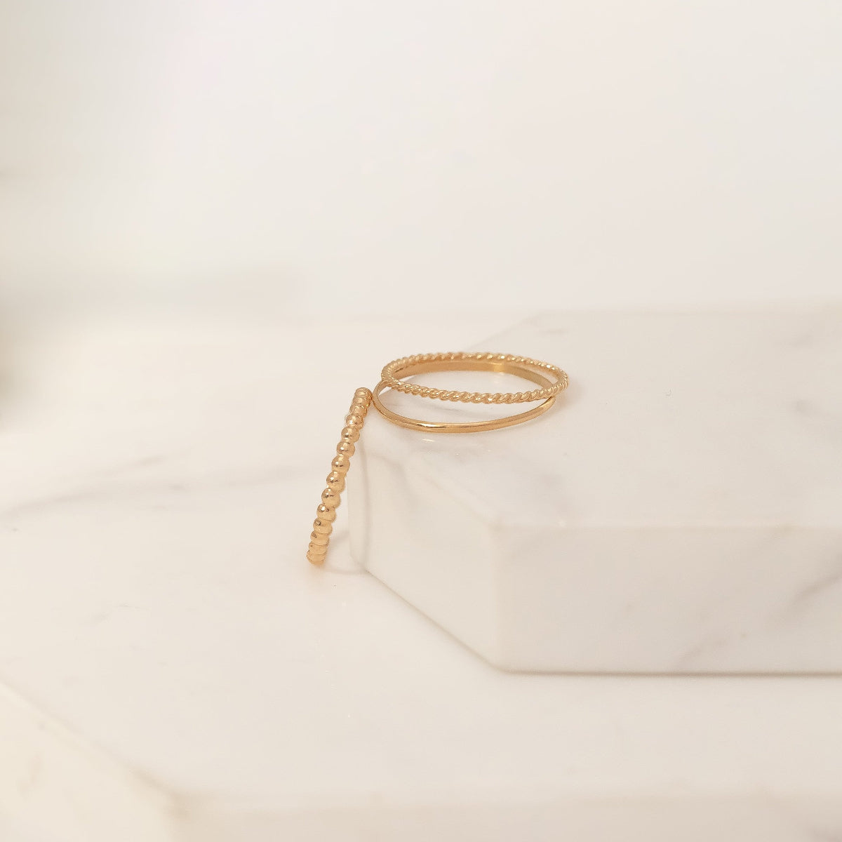 Yellow gold Delicate Trio Stacking Rings laid on a white marble surface and background. 