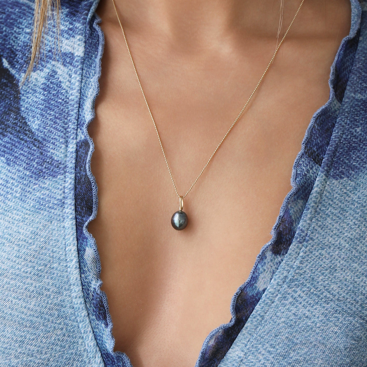 A close-up of a décolletage wearing a Baroque Pearl Necklace, styled in a blue top. 