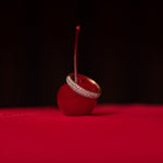 A Cosmo Ring on top of a cherry against a red and black background. 