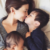 Woman holding two children close together and wearing a gold necklace with a letter M charm. 