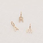 A Petite Letter Charm in m, Gold Letter Charm in A and a Pave Letter Charm R on a white textured background. 