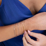 A close-up of a woman's wrist wearing mixed metal Element Short Link Bracelets and Element Long Link Bracelets, styled with a royal blue top. 