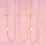 Three necklaces against a pink background -  Monogram Necklace with Heart Rose Gold and a W letter charm, a  Pavé Monogram Necklace with Diamond and a T letter charm, and a Monogram Necklace with Heart Yellow Gold and an S letter charm. 