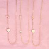 Three necklaces against a pink background -  Monogram Necklace with Heart Rose Gold and a W letter charm, a  Pavé Monogram Necklace with Diamond and a T letter charm, and a Monogram Necklace with Heart Yellow Gold and an S letter charm. 