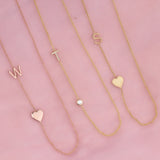 Three monogram necklaces against a pink background: a Monogram Necklace with Heart Rose Gold and a letter W charm, a Pavé Monogram Necklace with Diamond and a letter T charm in yellow gold and a Monogram Necklace with Heart Yellow Gold and a letter S charm.