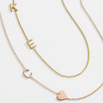 A yellow gold Custom Gold Necklace with two letters (K and E) and a Monogram Necklace with Heart Rose Gold with a letter C charm, against a white background.