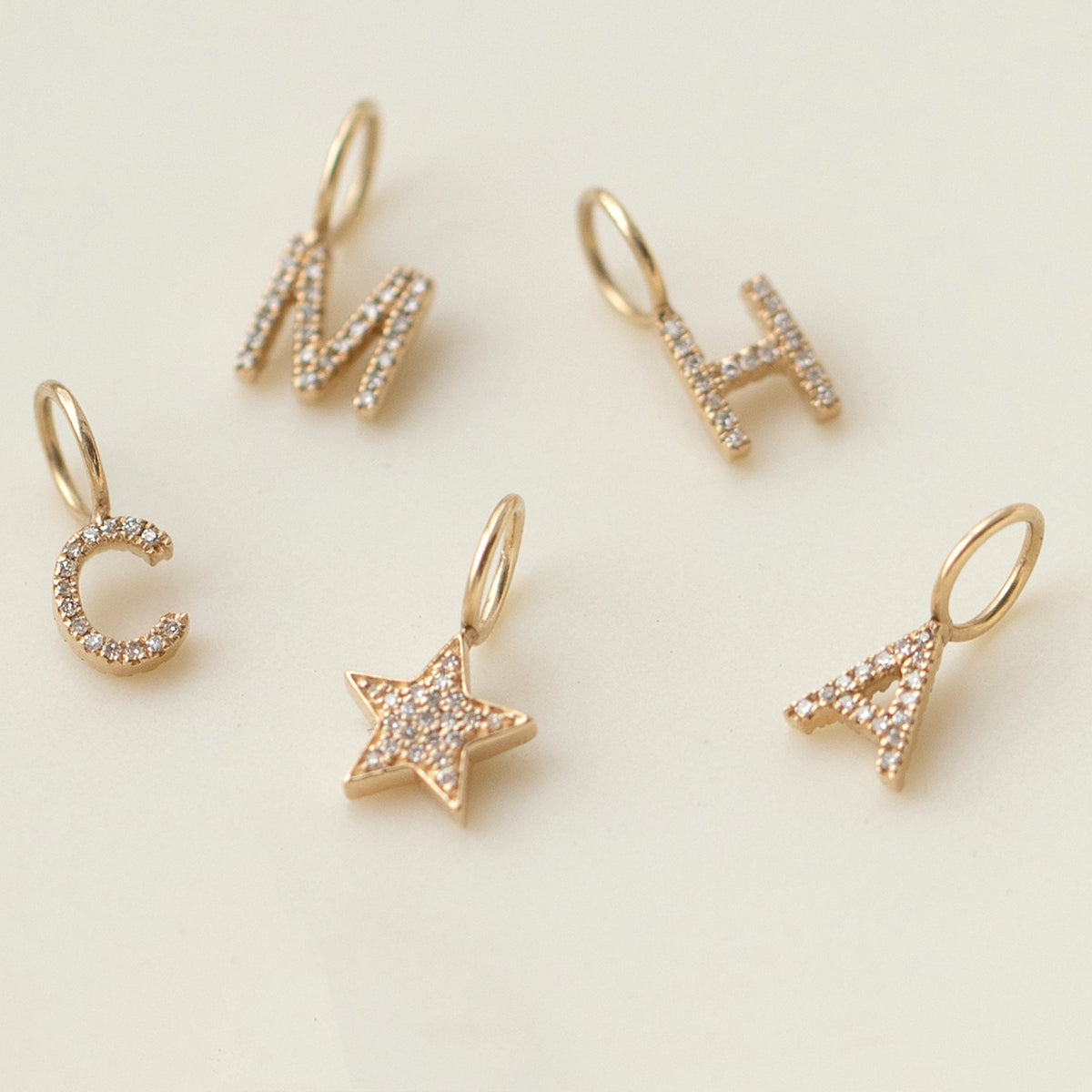 Pave Letter Charms in C, M, H and A and a Charm Pendant in Pave Star against a cream background. 