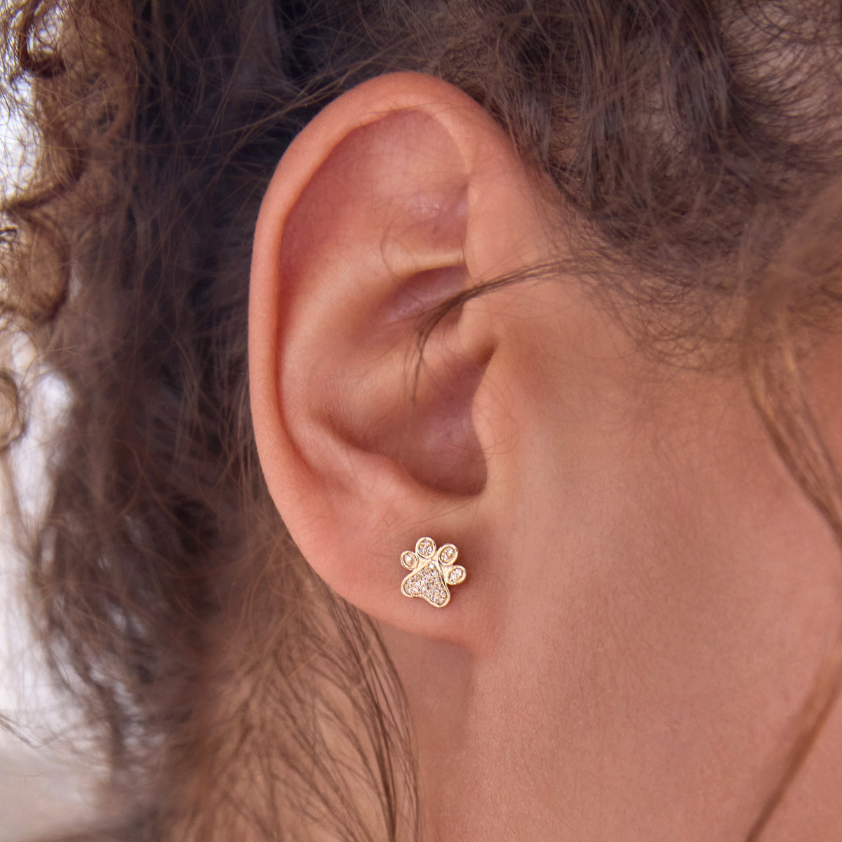 Close-up of an ear wearing a Pavé Charm Stud - Paw. 