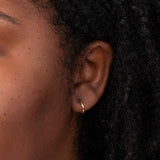 Close-up of a Thin Gold Hoop in a woman’s ear, with her black hair visible.
