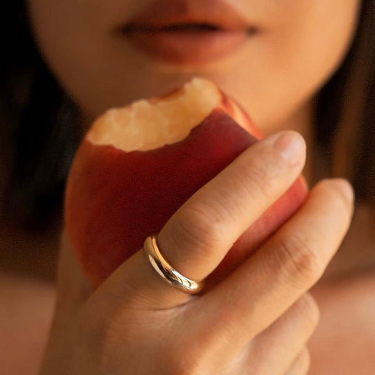 Close-up of a woman wearing a Tube Ring and holding a peach, with a softly blurred background. 