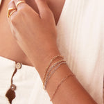 A close-up of a woman's wrist and hand wearing mixed metal Element Short Link Bracelets and Element Long Link Bracelets, and gold rings, styled with a white top. 