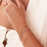 A close-up of a woman's wrist and hand wearing mixed metal Element Short Link Bracelets and Element Long Link Bracelets, and gold rings, styled with a white top. 
