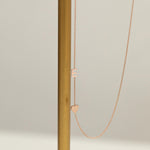A Monogram Necklace with Heart Rose Gold and a letter E charm next to a brown stick against a light grey background. 