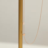 A Monogram Necklace with Heart Rose Gold and a letter E charm next to a brown stick against a light grey background. 