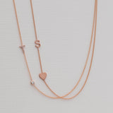 A Pavé Monogram Necklace with Diamond and a letter T charm in rose gold, and a Monogram Necklace with Heart Rose Gold and a letter S charm, against a neutral background.