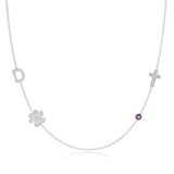 A Custom Gold Necklace in white gold with four charms, a pavé D and a paw positioned on the left side of the necklace, and a pavé cross and birthstone positioned on the right, on a white background.
