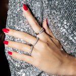 A hand wearing several white gold Cosmo Rings with red nails resting on a sequenced top. 