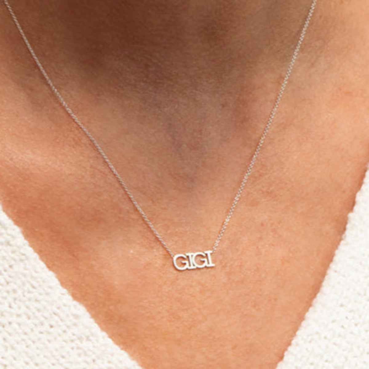 Close-up of a décolletage wearing a GIGI Necklace in white gold with a cable chain, with a white knit top. 
