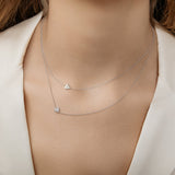 A close-up of a woman's neck wearing two white gold 14k Gold Asymmetrical Charm Necklaces in - Heart and Pavé Heart, styled in a white jacket. 
