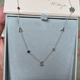 A Custom Gold Necklace in white gold with seven charms (two As, an S, three birthstones and a paw) in a Maya Brenner jewellery box. 