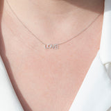 A close-up of a décolletage wearing a LOVE Necklace in white gold on a cable chain, with a white shirt.