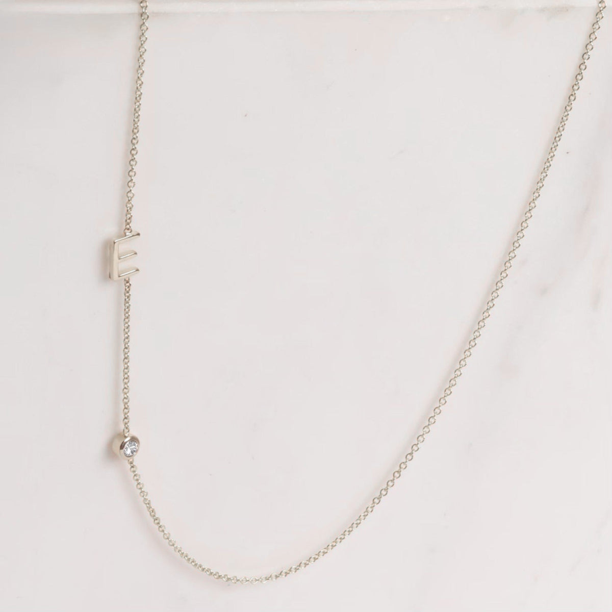 A Monogram Necklace with Diamond White Gold and a letter E charm on a light grey background. 