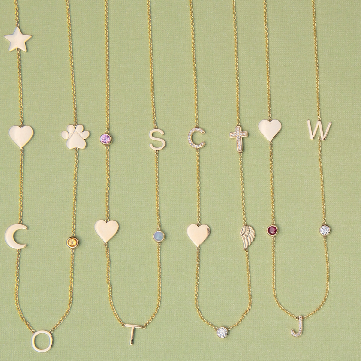 Four Custom Gold Necklaces in yellow gold, three with five different charms and one with six, laid against a light green background.