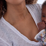 Woman holding a baby and wearing a yellow gold necklace with a P letter charm.