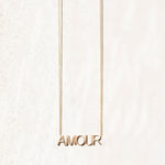 An AMOUR Necklace in yellow gold on a cable chain on an off-white background. 