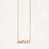 An AMOUR Necklace in yellow gold on a cable chain on an off-white background. 