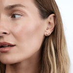 Close-up of a yellow gold Mini Preppy Post and Preppy Post in a brunette woman's ear against a white background. 