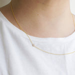 A close-up of a neck wearing a yellow gold 14K Gold Asymmetrical Birthstone Necklace - Diamond (April), styled in a white shirt. 